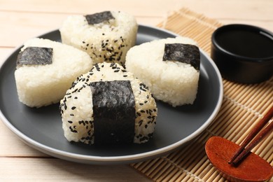 Photo of Rice balls (onigiri), soy sauce and chopsticks on wooden table, closeup. Traditional Japanese dish