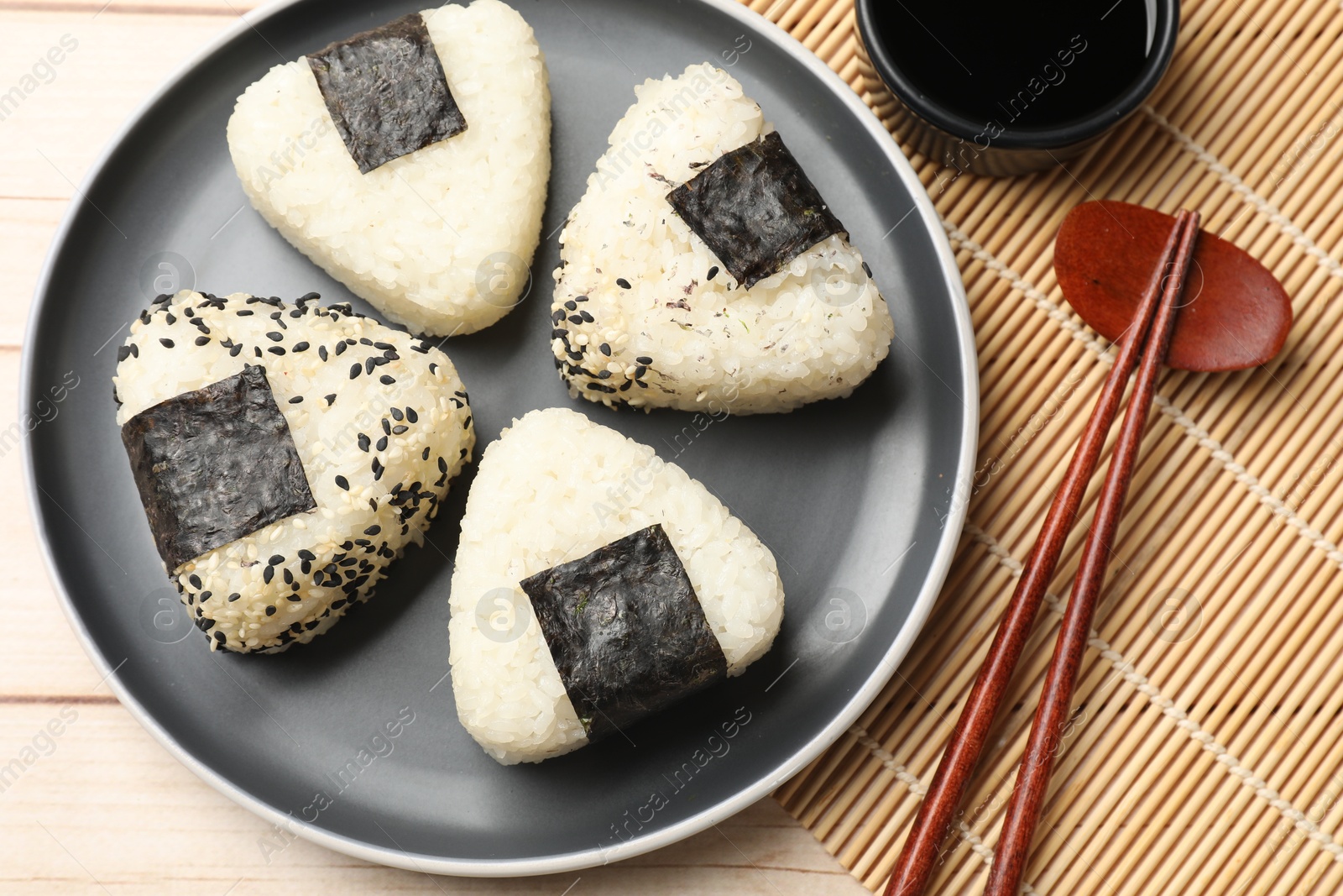 Photo of Rice balls (onigiri), soy sauce and chopsticks on wooden table, flat lay. Traditional Japanese dish