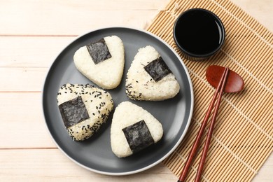 Photo of Rice balls (onigiri), soy sauce and chopsticks on wooden table, flat lay. Traditional Japanese dish