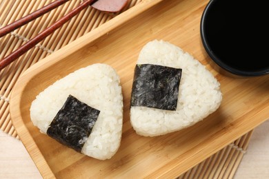 Photo of Rice balls (onigiri), soy sauce and chopsticks on table, flat lay. Traditional Japanese dish