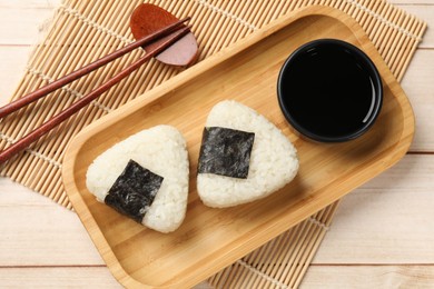 Photo of Rice balls (onigiri), soy sauce and chopsticks on wooden table, flat lay. Traditional Japanese dish