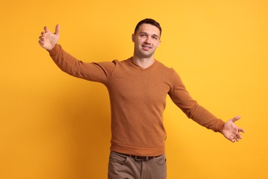 Photo of Cheerful man welcoming guests on orange background