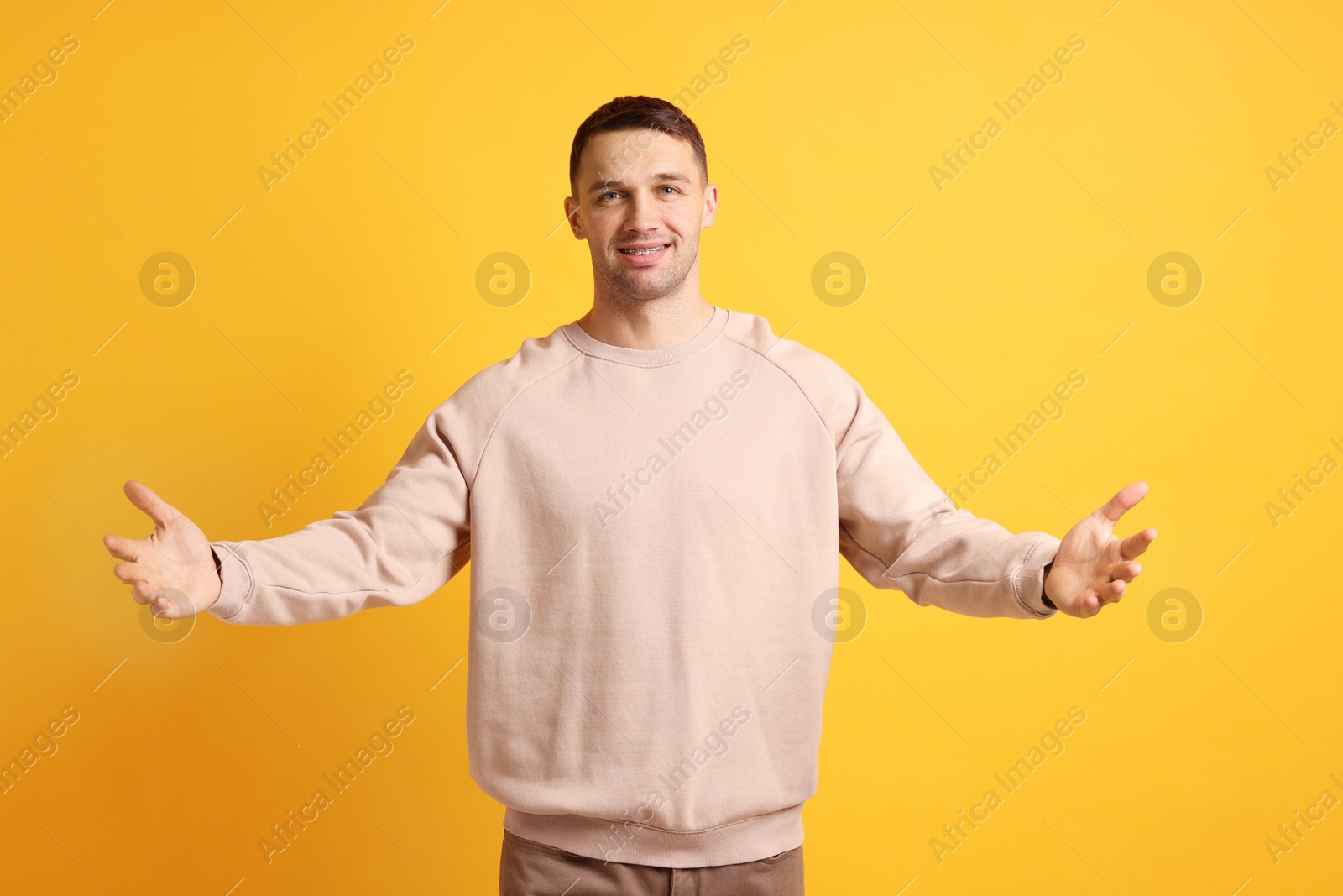 Photo of Cheerful man welcoming guests on orange background