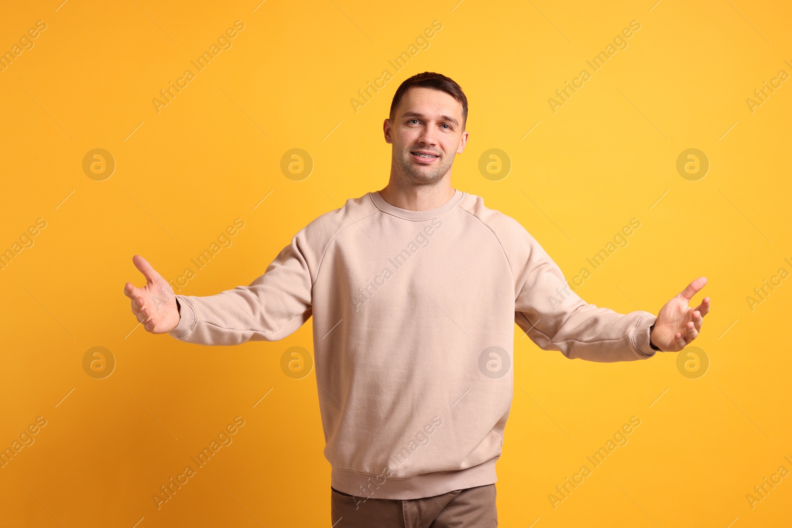 Photo of Cheerful man welcoming guests on orange background