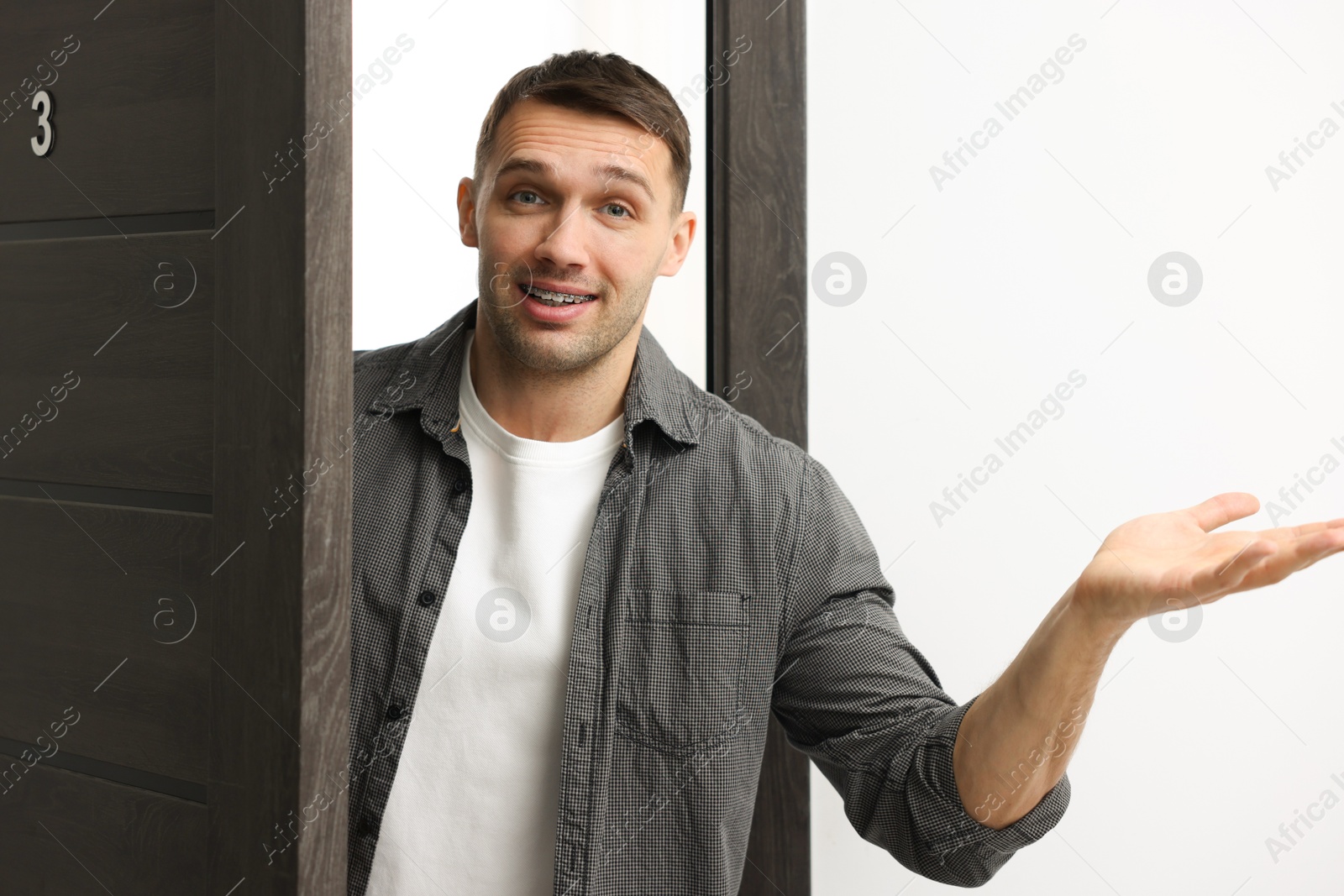 Photo of Cheerful man meeting guests in doorway of his apartment