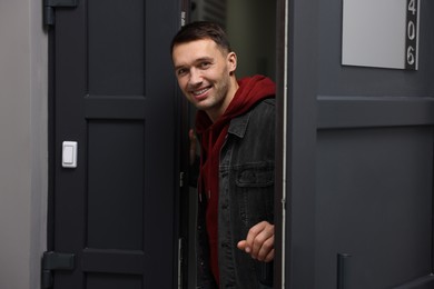 Photo of Cheerful man meeting guests in doorway of his apartment