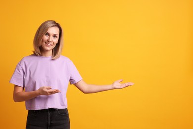 Photo of Cheerful woman welcoming guests on orange background. Space for text