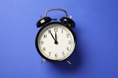 Photo of One black alarm clock on blue background, top view