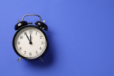Photo of One black alarm clock on blue background, top view. Space for text