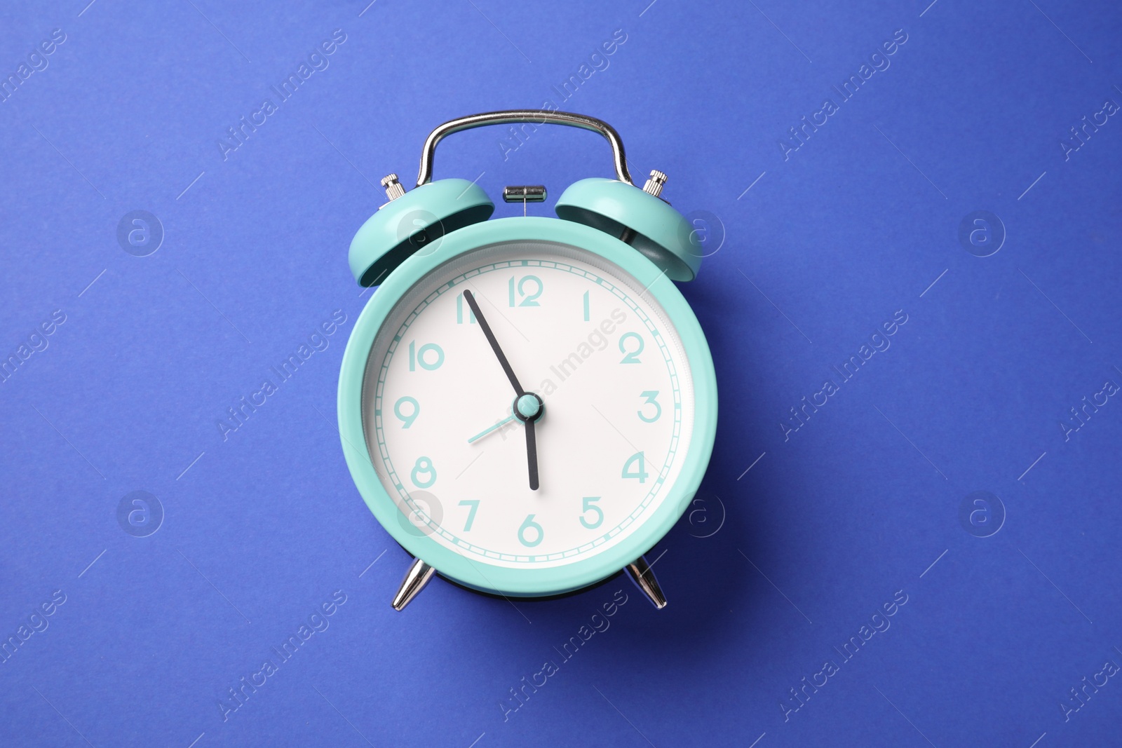One turquoise alarm clock on blue background, top view Photo of One turquoise alarm clock on blue background, top view