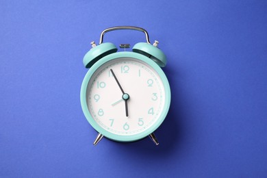 Photo of One turquoise alarm clock on blue background, top view