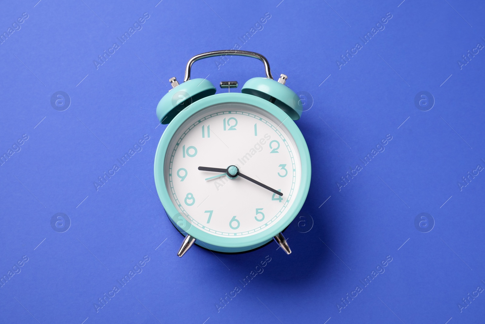 One turquoise alarm clock on blue background, top view Photo of One turquoise alarm clock on blue background, top view