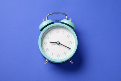 Photo of One turquoise alarm clock on blue background, top view