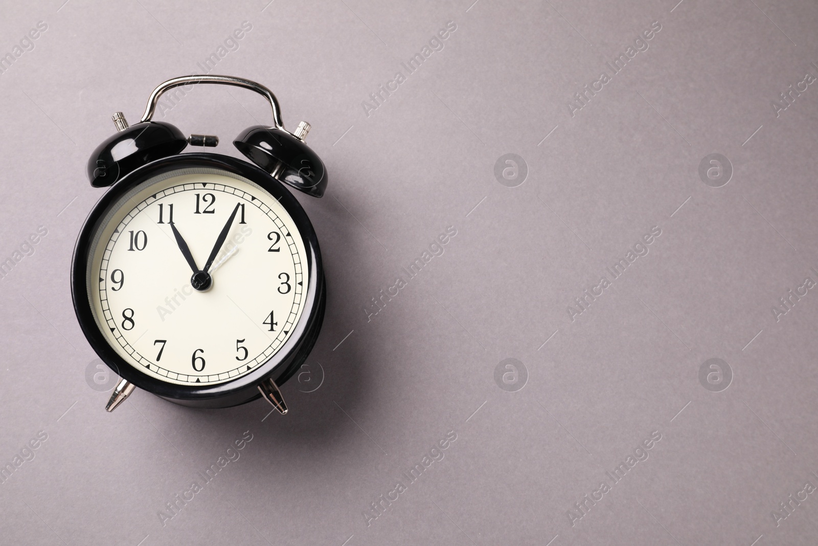 Photo of One black alarm clock on light grey background, top view. Space for text