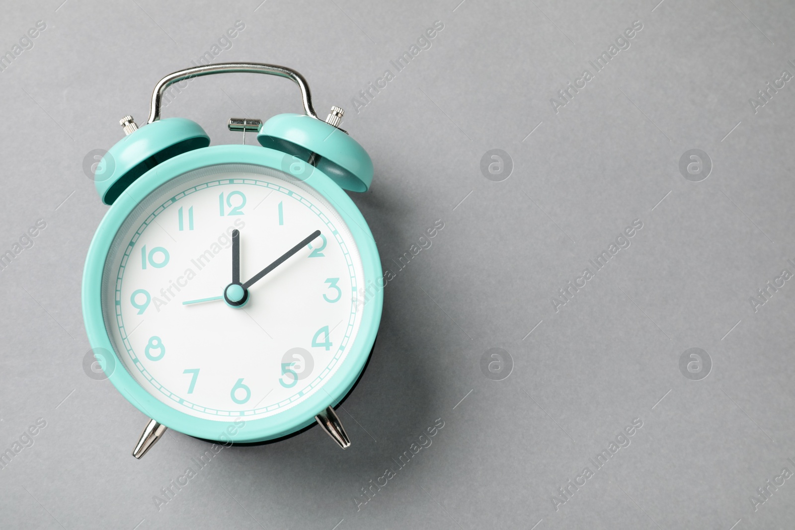Photo of One turquoise alarm clock on light grey background, top view. Space for text