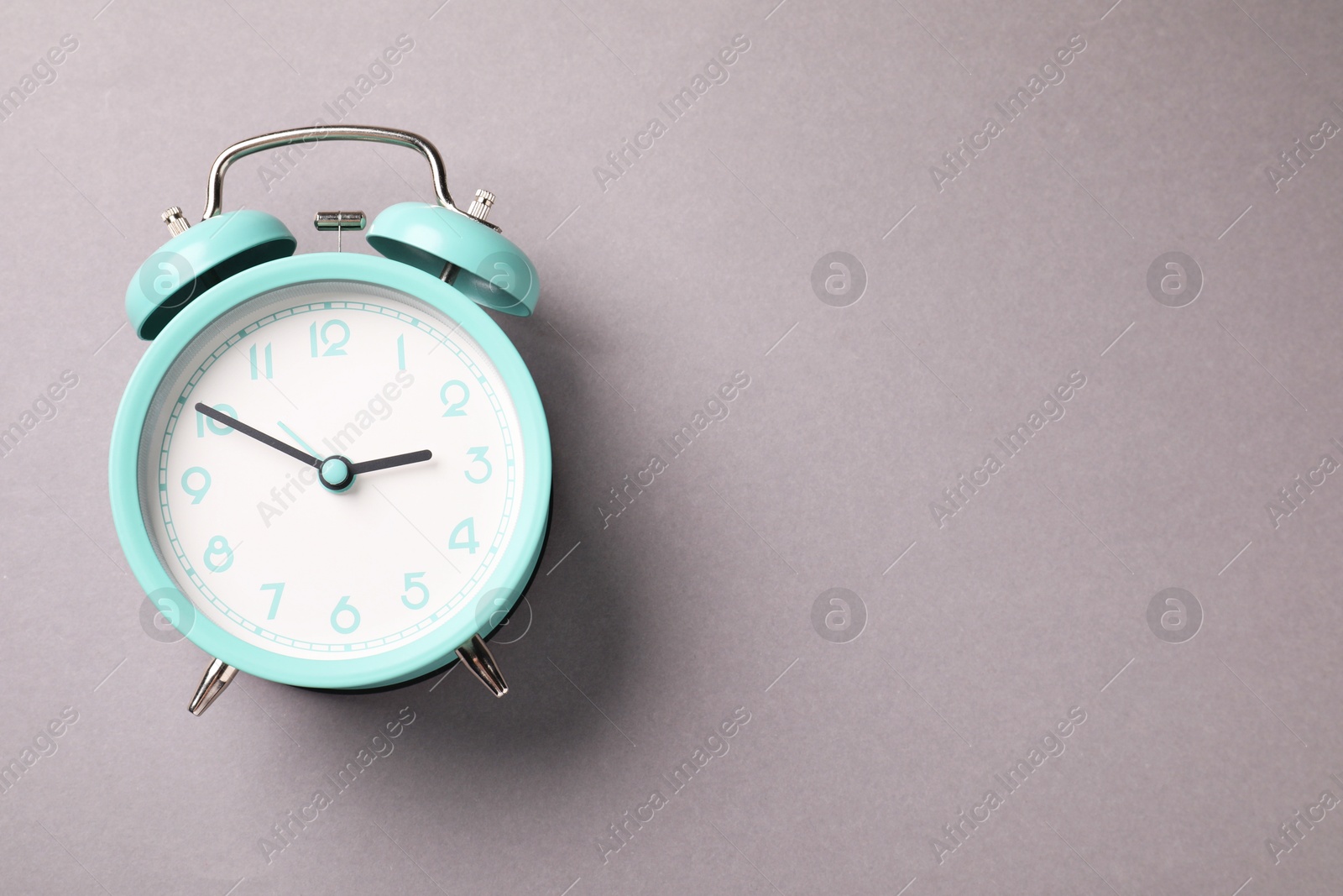 Photo of One turquoise alarm clock on light grey background, top view. Space for text