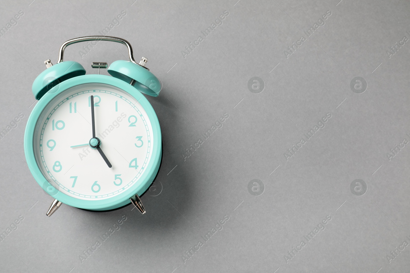 Photo of One turquoise alarm clock on light grey background, top view. Space for text