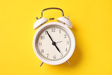 Photo of White alarm clock on yellow background, top view