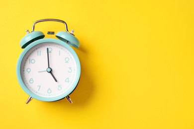 Photo of Turquoise alarm clock on yellow background, top view. Space for text