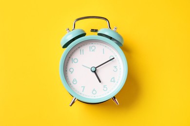 Photo of Turquoise alarm clock on yellow background, top view