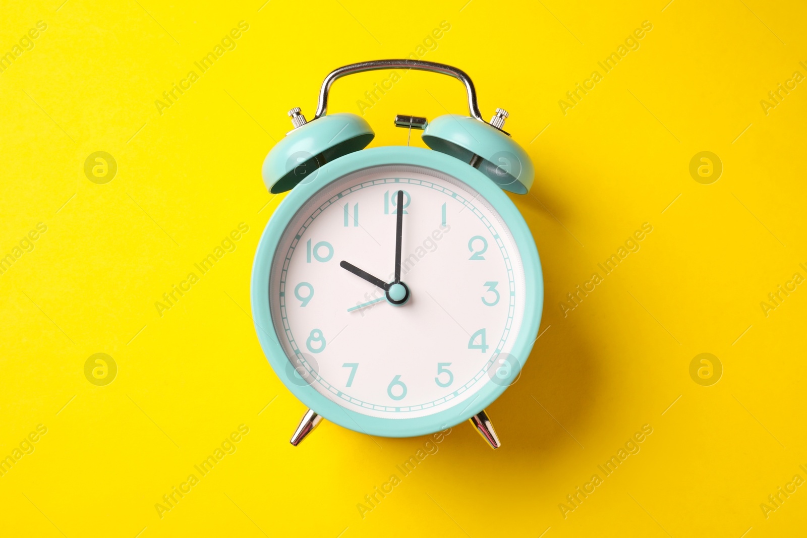 Turquoise alarm clock on yellow background, top view Photo of Turquoise alarm clock on yellow background, top view