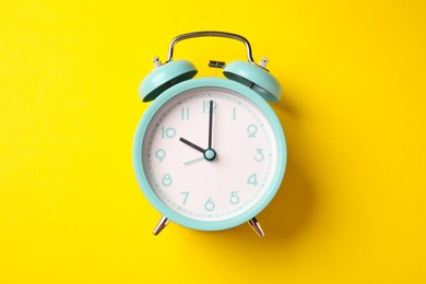 Photo of Turquoise alarm clock on yellow background, top view