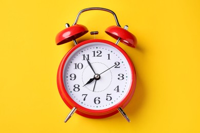 Photo of Red alarm clock on yellow background, top view