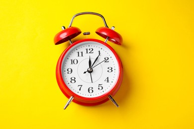 Photo of Red alarm clock on yellow background, top view