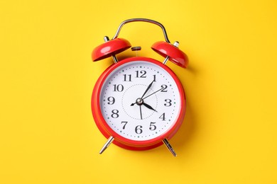 Photo of Red alarm clock on yellow background, top view