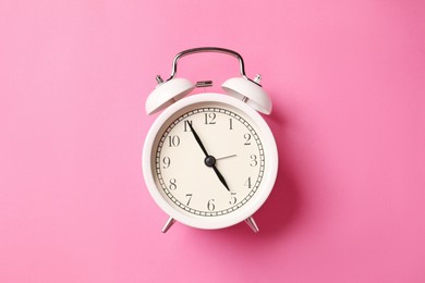 Photo of White alarm clock on pink background, top view