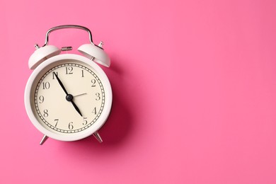 Photo of White alarm clock on pink background, top view. Space for text