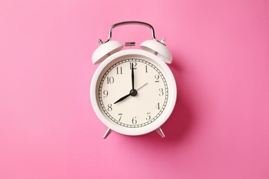 Photo of White alarm clock on pink background, top view