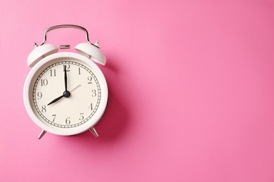 Photo of White alarm clock on pink background, top view. Space for text