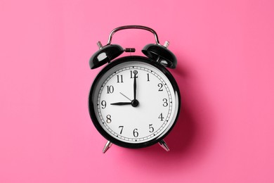 Photo of Black alarm clock on pink background, top view