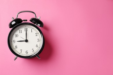 Photo of Black alarm clock on pink background, top view. Space for text