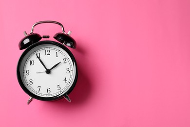 Photo of Black alarm clock on pink background, top view. Space for text
