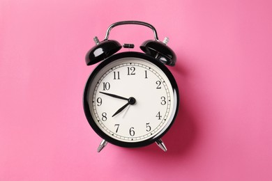 Photo of Black alarm clock on pink background, top view
