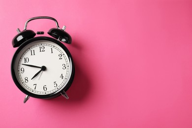 Photo of Black alarm clock on pink background, top view. Space for text