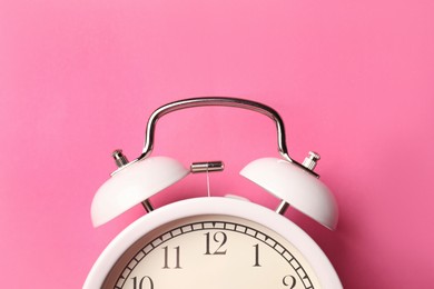 Photo of White alarm clock on pink background, top view