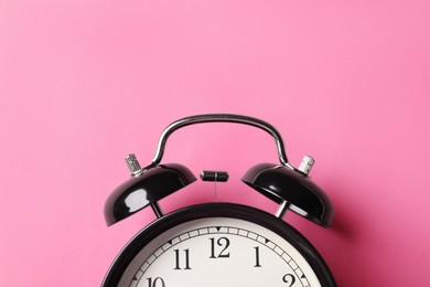Photo of Black alarm clock on pink background, top view