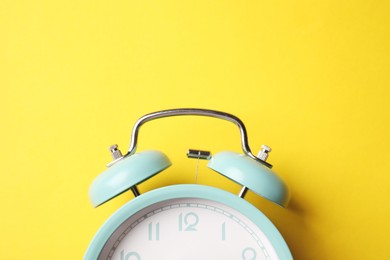 Photo of Turquoise alarm clock on yellow background, top view