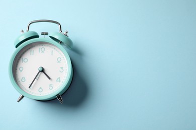 Photo of Turquoise alarm clock on light blue background, top view. Space for text