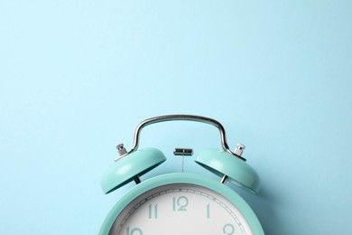 Photo of Turquoise alarm clock on light blue background, top view. Space for text