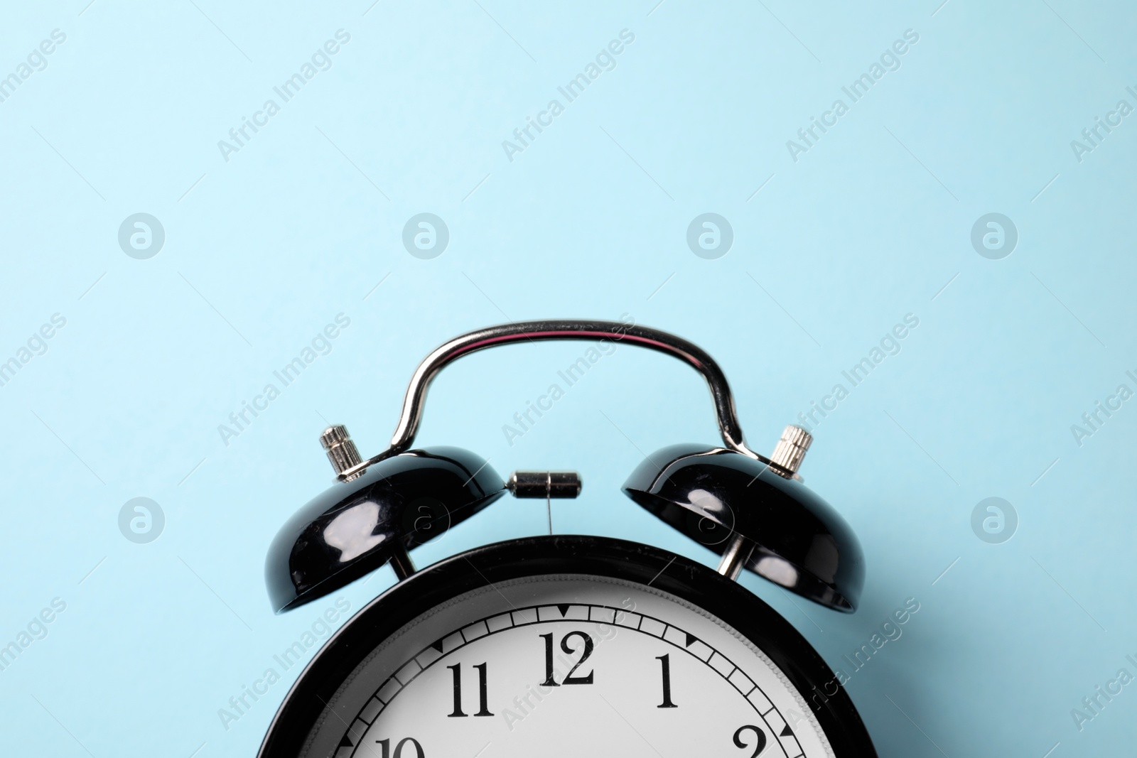 Black alarm clock on light blue background, top view. Space for text Photo of Black alarm clock on light blue background, top view. Space for text