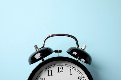 Photo of Black alarm clock on light blue background, top view. Space for text