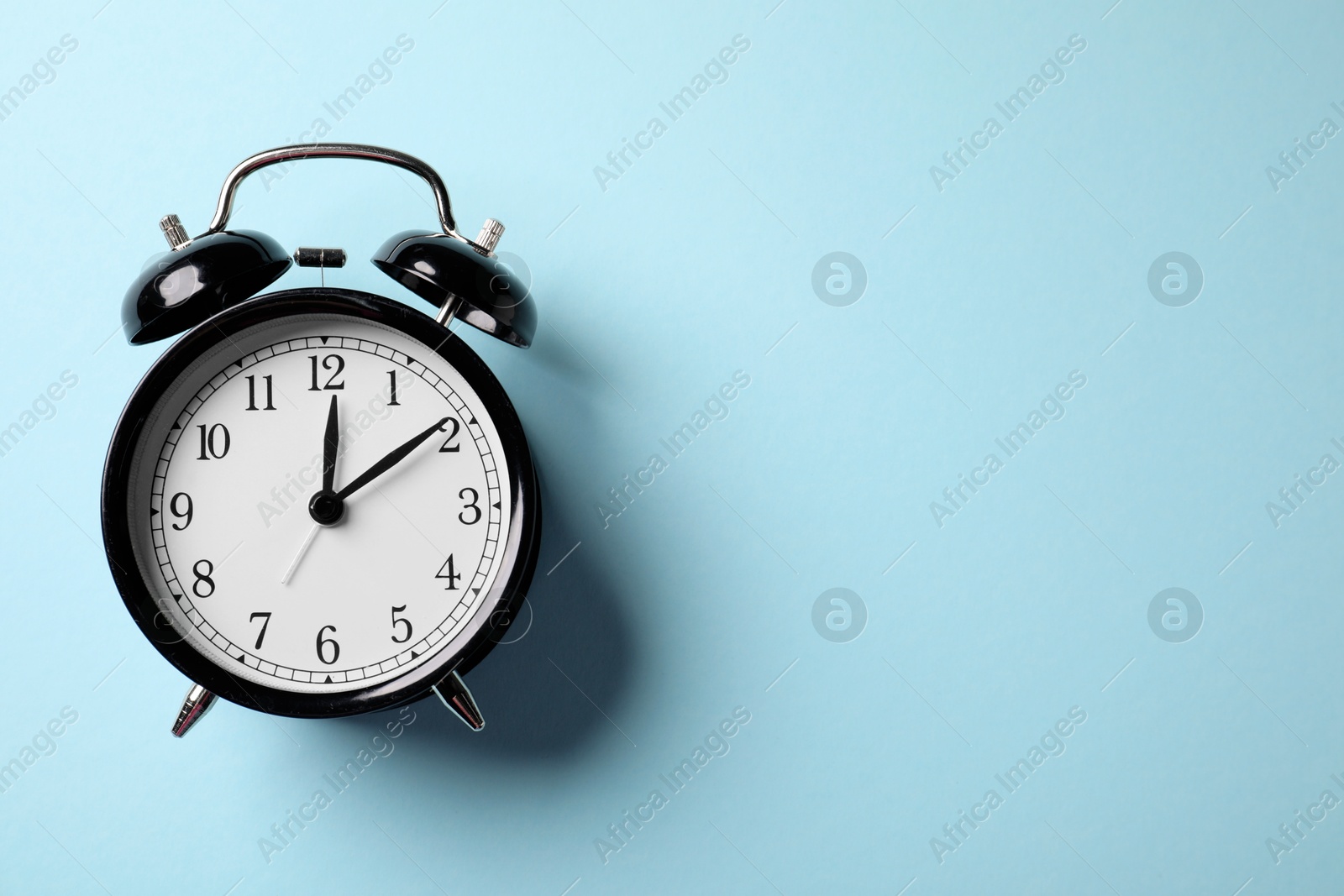 Black alarm clock on light blue background, top view. Space for text Photo of Black alarm clock on light blue background, top view. Space for text
