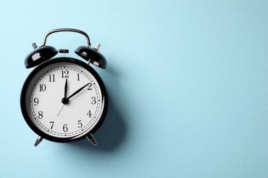 Photo of Black alarm clock on light blue background, top view. Space for text