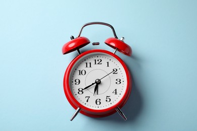 Photo of Red alarm clock on light blue background, top view