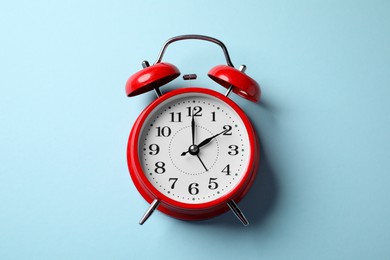 Photo of Red alarm clock on light blue background, top view