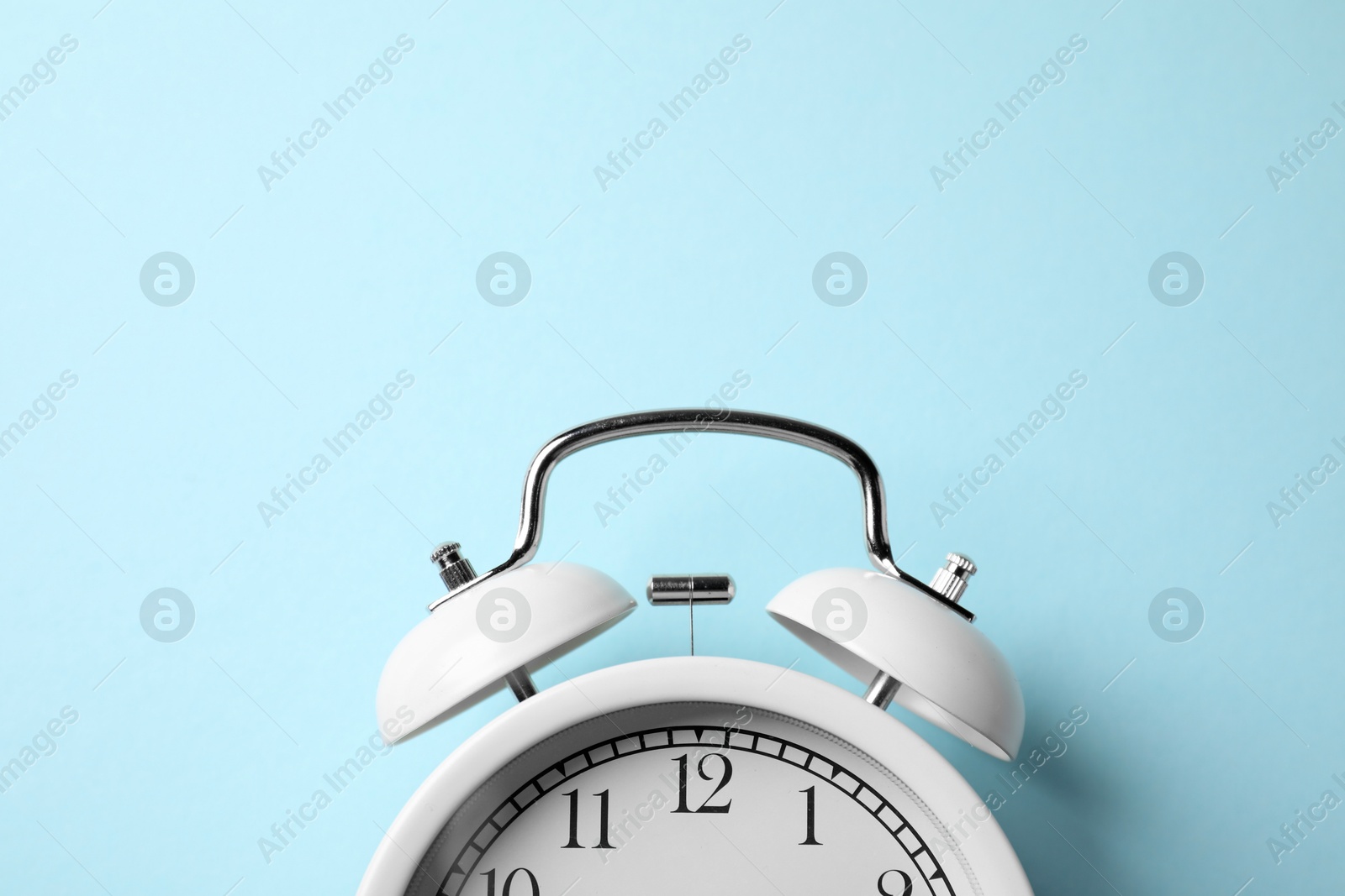 White alarm clock on light blue background, top view. Space for text Photo of White alarm clock on light blue background, top view. Space for text